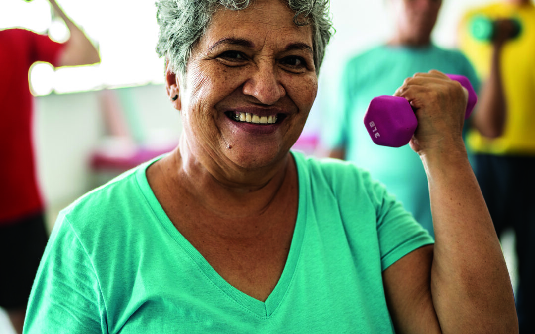 Portrait of senior woman lifting weights with classmates at the gym